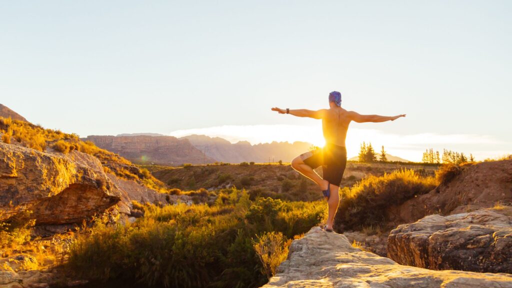 Mann mit nacktem Oberkörper macht Yoga in Berglandschaft